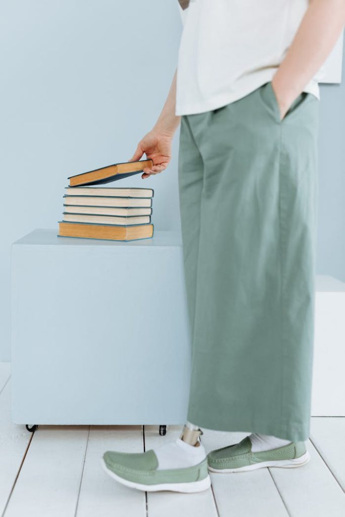 a-person-with-prosthetic-leg-8011894 Person with green pants and prosthetic leg standing next to a stack of books.