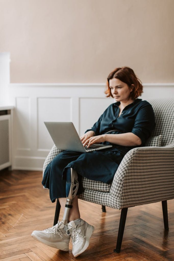 Woman with a prosthetic leg working from home on her laptop, sitting indoors.