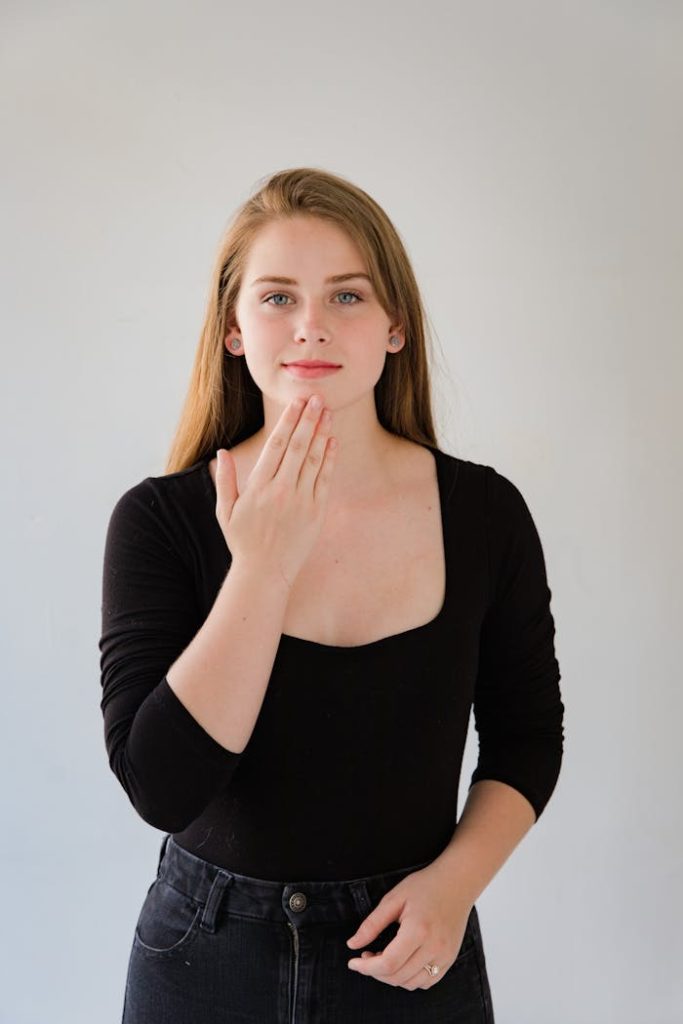 A young woman with long hair using sign language against a neutral background.